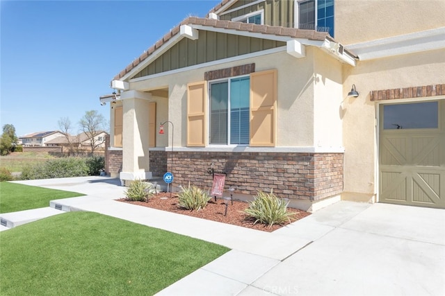 view of exterior entry with a yard, stucco siding, a garage, stone siding, and board and batten siding