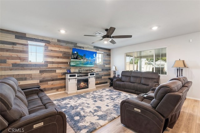 living area with light wood finished floors, a healthy amount of sunlight, an accent wall, and a lit fireplace