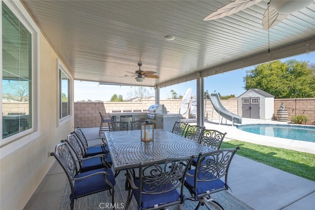 view of patio with an outbuilding, outdoor dining area, a fenced backyard, ceiling fan, and a storage shed