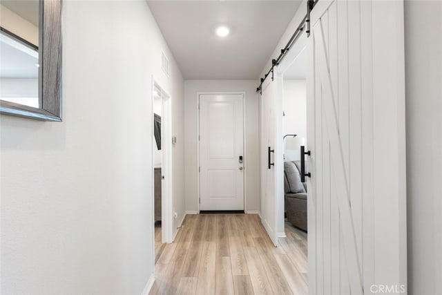 hall featuring light wood finished floors, visible vents, baseboards, and a barn door