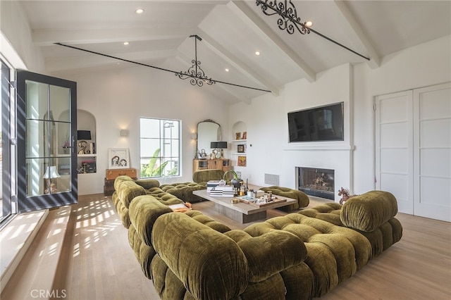 living area with beamed ceiling, wood finished floors, high vaulted ceiling, and a glass covered fireplace