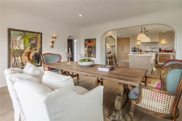 dining area with recessed lighting, arched walkways, and light wood finished floors