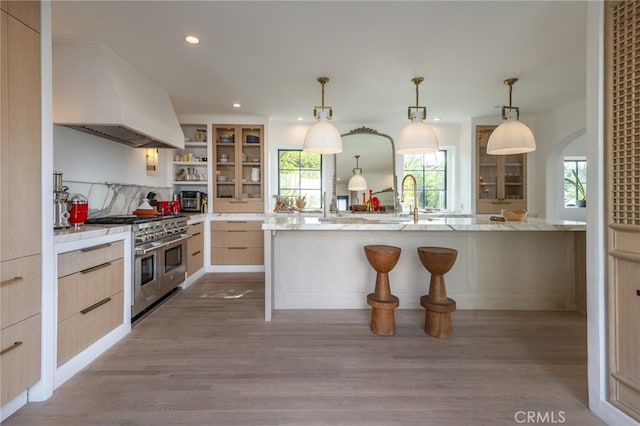 kitchen featuring a breakfast bar area, wood finished floors, double oven range, light brown cabinets, and custom exhaust hood