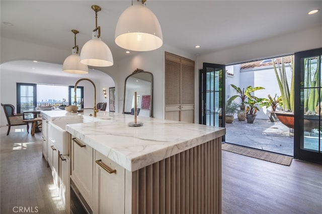 kitchen featuring a kitchen island with sink, decorative light fixtures, wood finished floors, recessed lighting, and light stone countertops