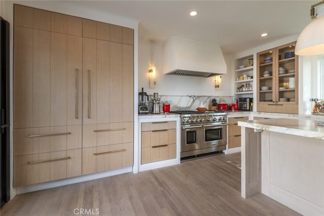 kitchen featuring wood finished floors, double oven range, modern cabinets, and premium range hood