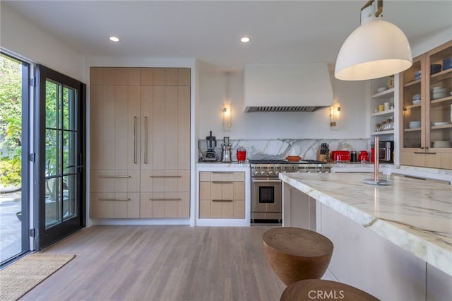 kitchen with light wood finished floors, high end stainless steel range, custom range hood, and light stone countertops