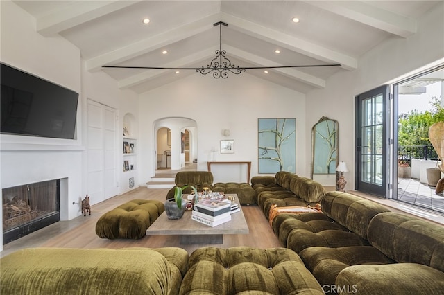 living area featuring built in shelves, vaulted ceiling with beams, light wood-style flooring, and a fireplace