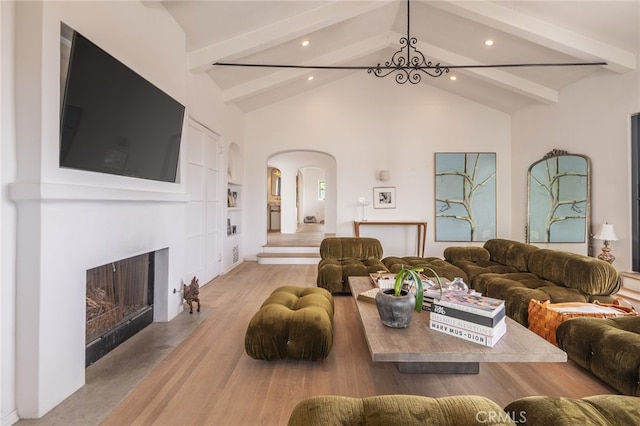 living area with beamed ceiling, a fireplace with flush hearth, wood finished floors, and arched walkways