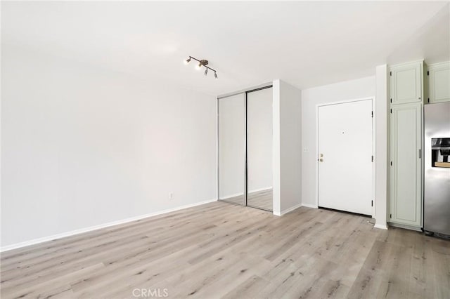 unfurnished bedroom featuring light wood-style flooring, baseboards, stainless steel refrigerator with ice dispenser, and a closet