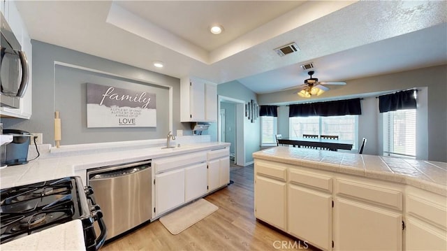 kitchen featuring visible vents, light wood-type flooring, a tray ceiling, appliances with stainless steel finishes, and a sink