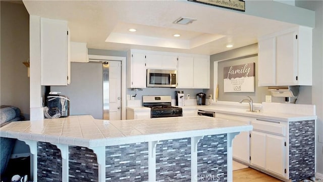 kitchen featuring stainless steel microwave, visible vents, range with gas cooktop, white cabinetry, and a raised ceiling