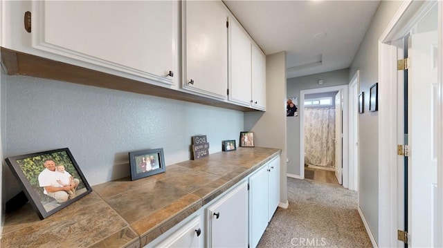 interior space with light colored carpet, white cabinetry, tile countertops, and baseboards