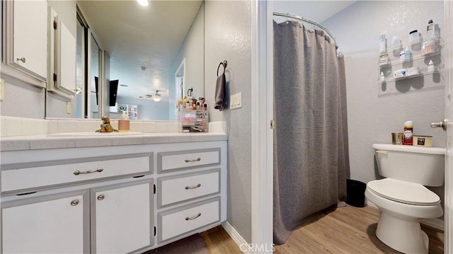 bathroom with curtained shower, toilet, wood finished floors, a textured wall, and vanity