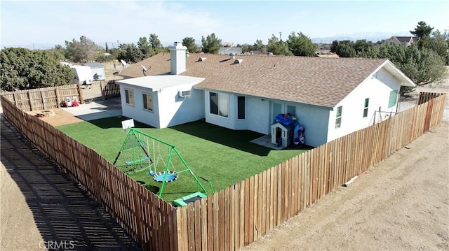 back of property with a shingled roof, a playground, a lawn, stucco siding, and a fenced backyard