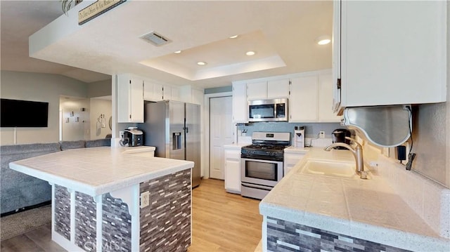 kitchen featuring appliances with stainless steel finishes, light wood-type flooring, a peninsula, and a sink