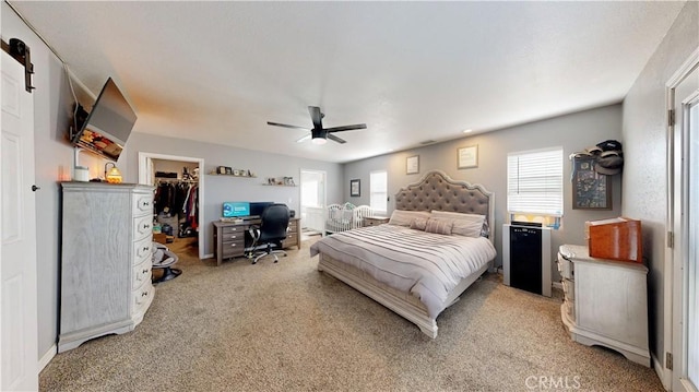 bedroom with a spacious closet, light carpet, a closet, refrigerator, and a ceiling fan