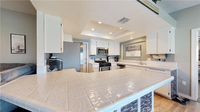 kitchen featuring visible vents, a tray ceiling, recessed lighting, light wood-style flooring, and stainless steel appliances