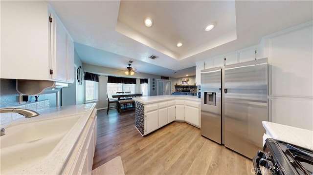 kitchen with a peninsula, stainless steel fridge with ice dispenser, a sink, white cabinets, and a raised ceiling