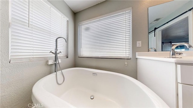 full bath featuring a soaking tub, vanity, and a textured wall