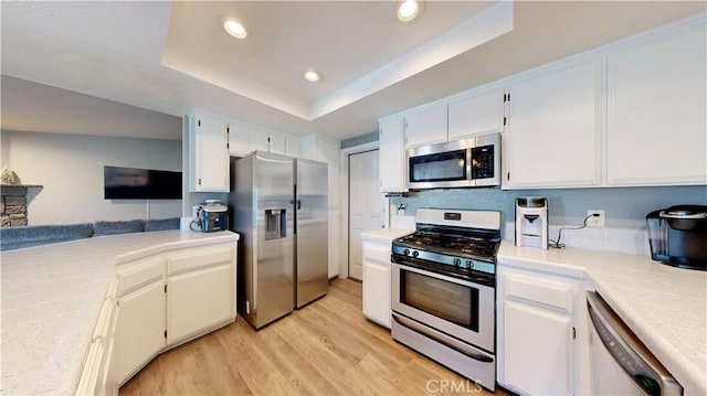 kitchen with a tray ceiling, light wood-style flooring, light countertops, and stainless steel appliances