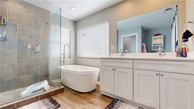 full bathroom with a shower stall, a freestanding tub, wood finished floors, and double vanity