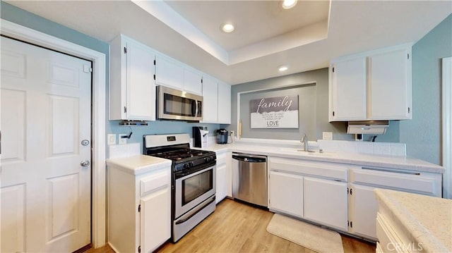 kitchen with white cabinets, stainless steel appliances, light countertops, and a sink