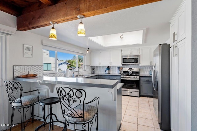 kitchen featuring a peninsula, white cabinets, backsplash, and appliances with stainless steel finishes