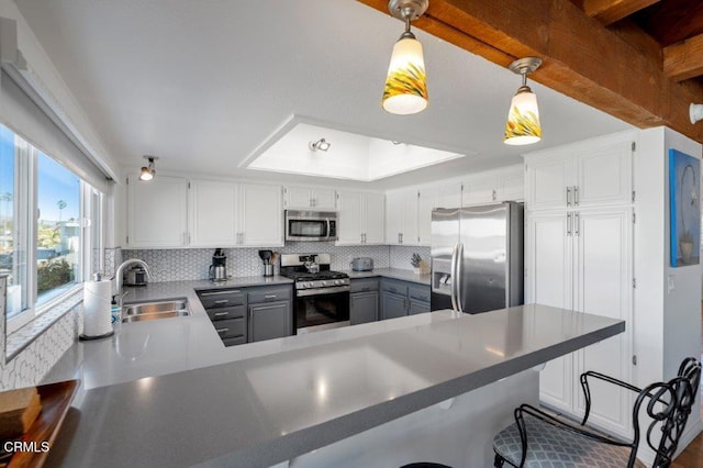 kitchen with decorative backsplash, gray cabinets, a peninsula, stainless steel appliances, and a sink