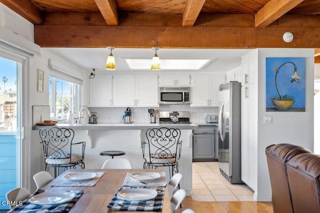 kitchen featuring a peninsula, beamed ceiling, backsplash, and appliances with stainless steel finishes