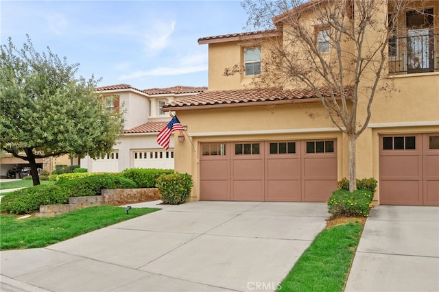 mediterranean / spanish home featuring a tile roof, stucco siding, an attached garage, and concrete driveway