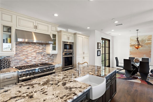 kitchen with visible vents, a sink, stainless steel appliances, under cabinet range hood, and cream cabinets