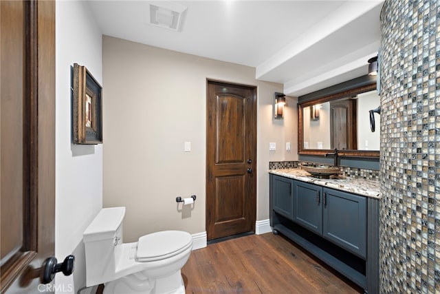 bathroom featuring visible vents, baseboards, toilet, wood finished floors, and vanity