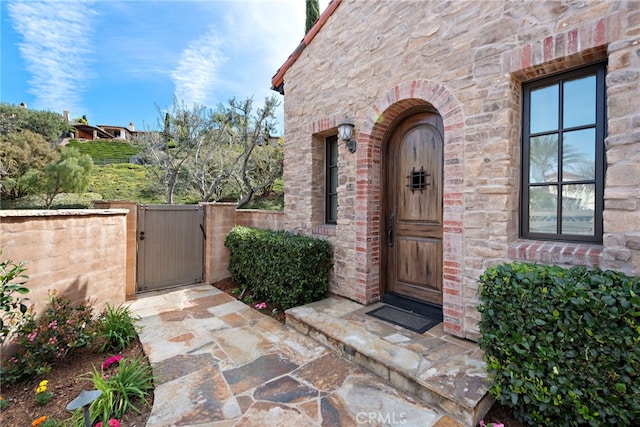 doorway to property featuring a gate, fence, and stone siding