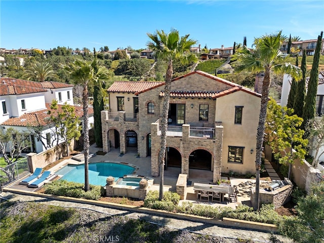 back of house with a patio, a balcony, stone siding, and a pool with connected hot tub