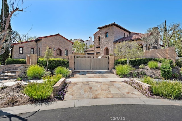 mediterranean / spanish-style house with a tiled roof, a gate, driveway, and a fenced front yard