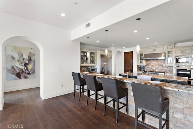 kitchen featuring under cabinet range hood, built in appliances, arched walkways, and visible vents