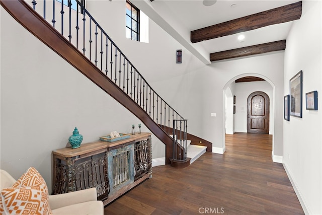 foyer entrance featuring baseboards, beamed ceiling, stairway, wood finished floors, and arched walkways