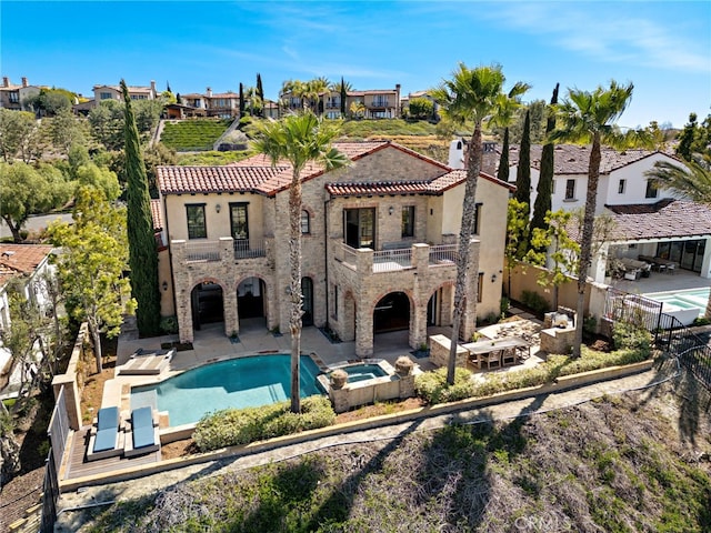 back of property with a patio, a fenced backyard, a balcony, an outdoor pool, and an in ground hot tub