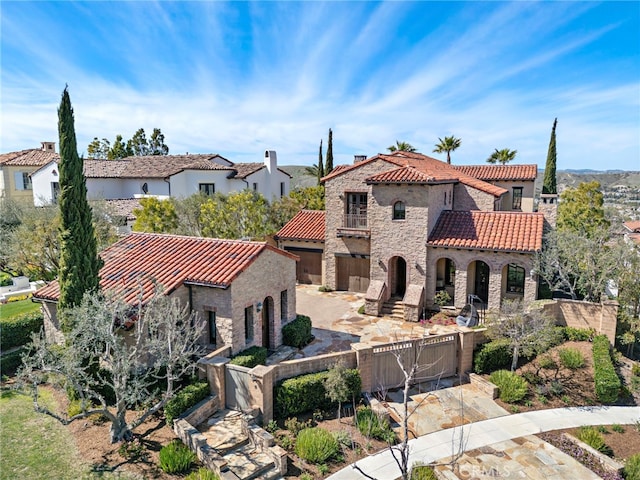 mediterranean / spanish-style house featuring a fenced front yard, stone siding, concrete driveway, a balcony, and a tiled roof