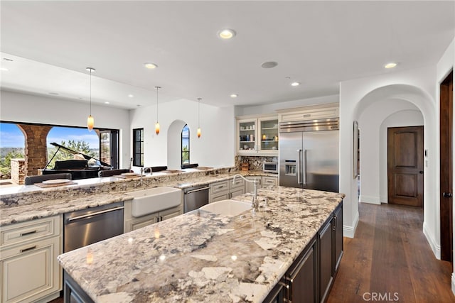 kitchen featuring a sink, glass insert cabinets, arched walkways, and appliances with stainless steel finishes