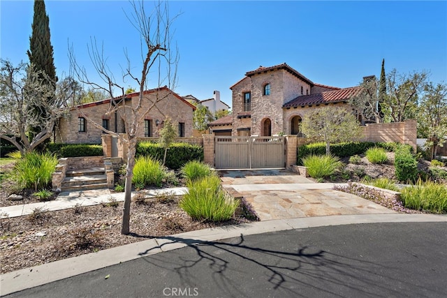 mediterranean / spanish-style house featuring a gate, driveway, stucco siding, a fenced front yard, and a tile roof