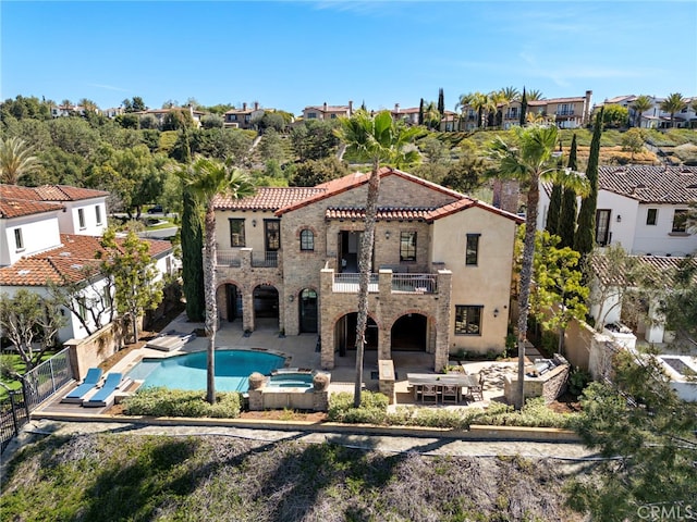 back of property featuring a pool with connected hot tub, stone siding, a patio, a fenced backyard, and a balcony