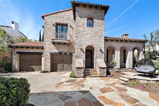 mediterranean / spanish house featuring a tiled roof, a balcony, a garage, and driveway