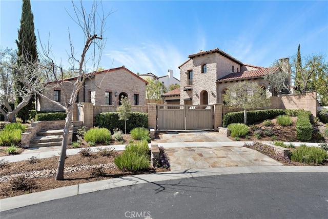 mediterranean / spanish house with a gate, driveway, stucco siding, a fenced front yard, and a tile roof