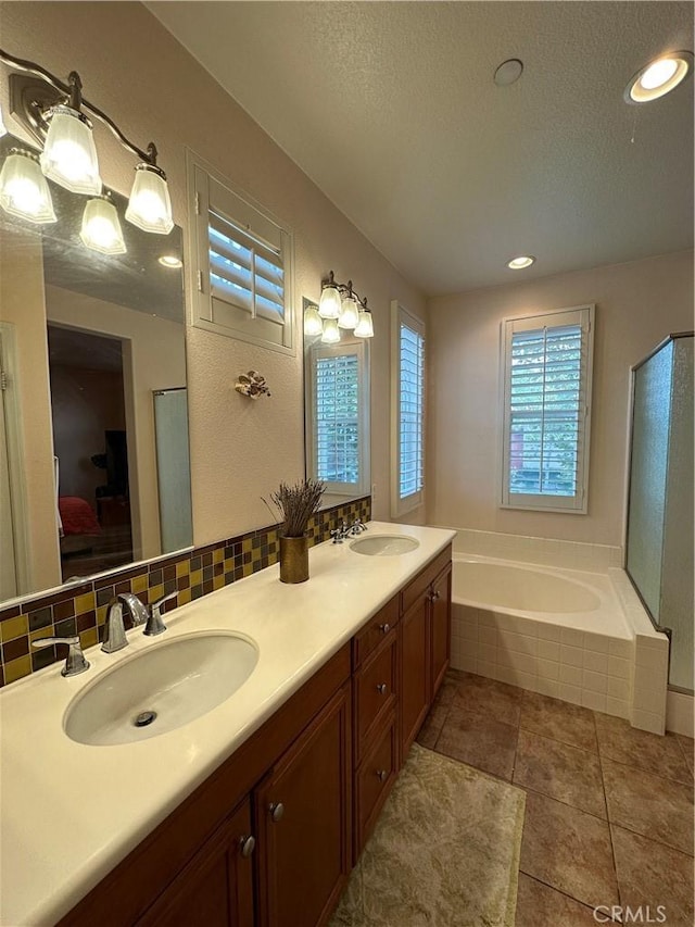 ensuite bathroom with double vanity, decorative backsplash, a garden tub, and a sink