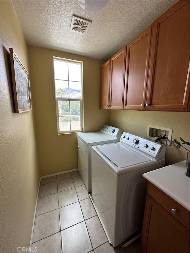 washroom featuring visible vents, light tile patterned flooring, cabinet space, a textured ceiling, and washer and clothes dryer