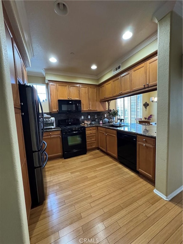 kitchen featuring visible vents, crown molding, light wood-style flooring, brown cabinets, and black appliances