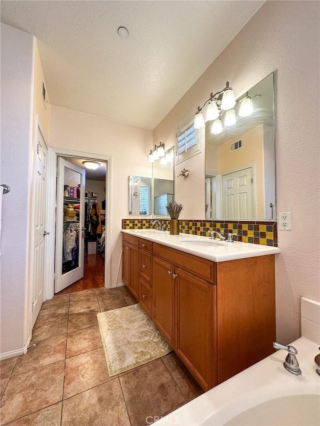 bathroom with visible vents, double vanity, a sink, a textured ceiling, and backsplash