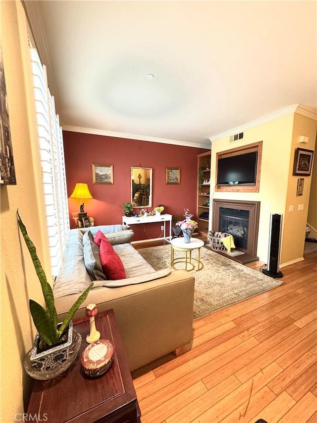 living area featuring visible vents, baseboards, ornamental molding, wood finished floors, and a glass covered fireplace