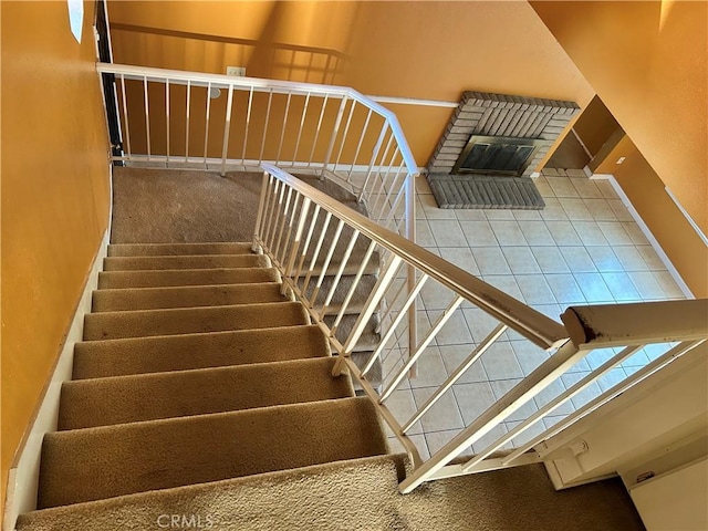 stairway featuring tile patterned floors, a brick fireplace, baseboards, and carpet floors